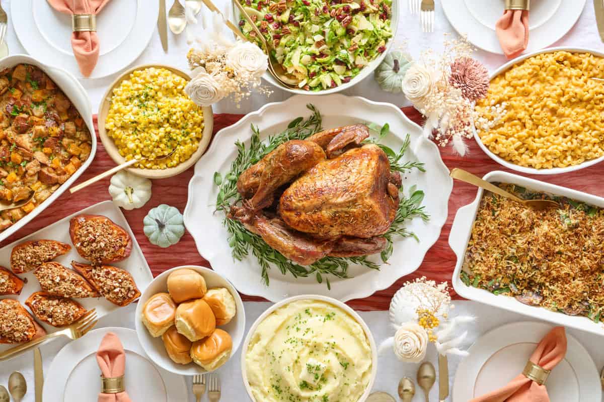Feel Good Foodie's Thanksgiving table with turkey, mac and cheese, mashed potatoes, green bean casserole, sweet potatoes, brussel sprouts salad, creamed corn, and stuffing.