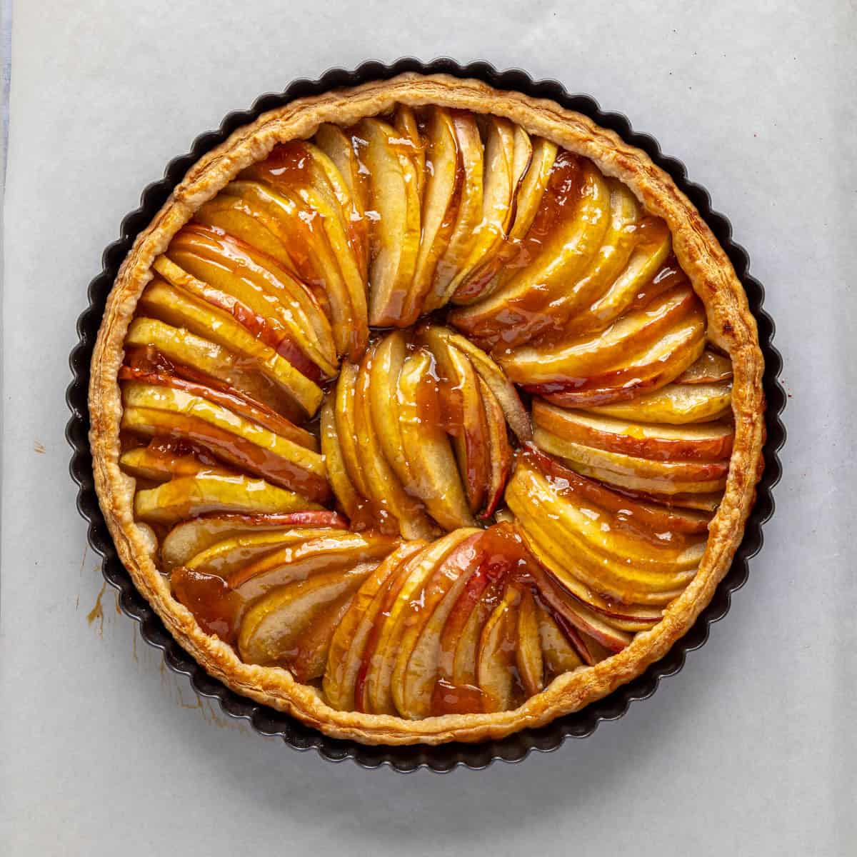 After apple puff pastry tart has baked with apricot jam brushed on top.