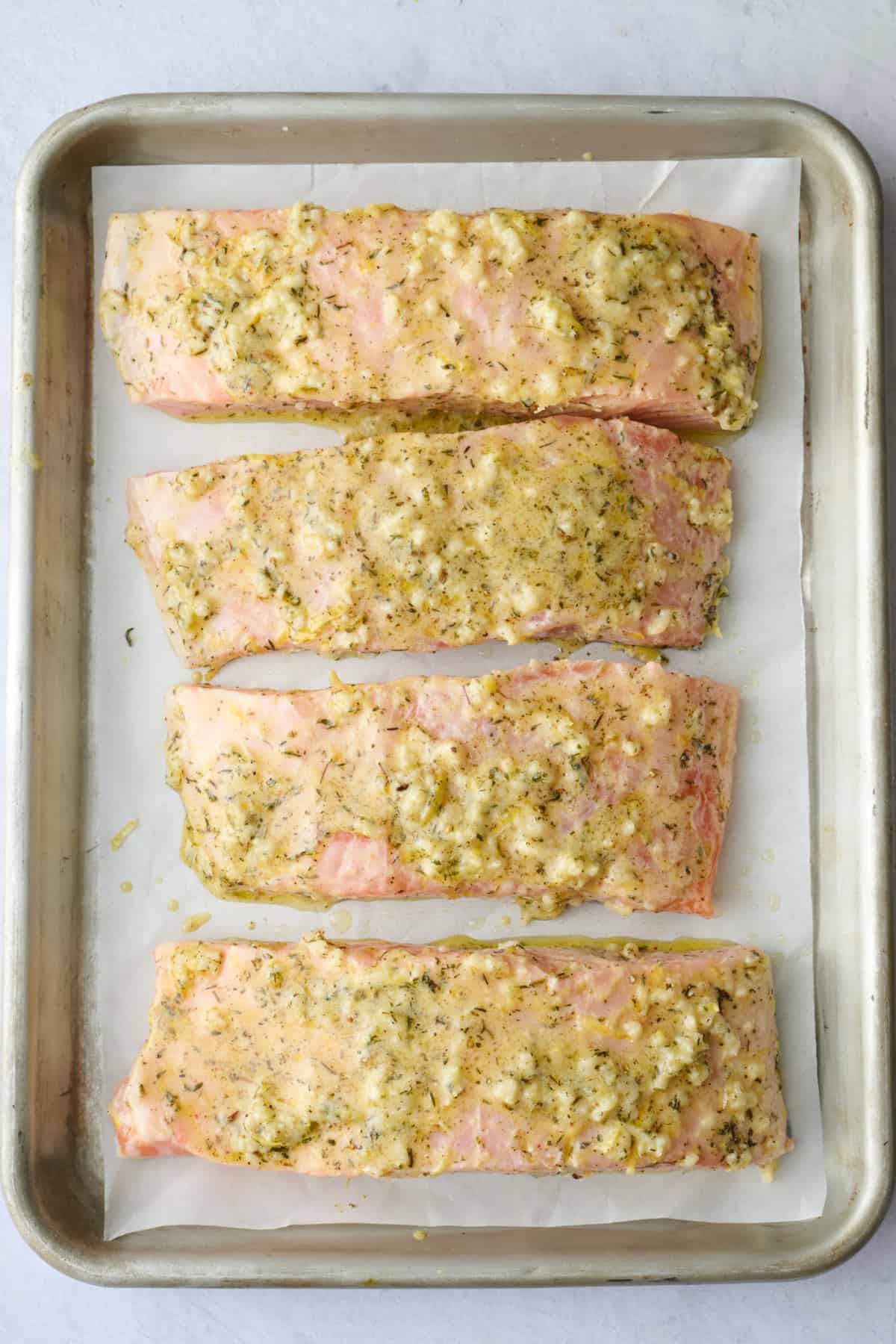 Marinated salmon skin side down on a prepared baking sheet with extra marinade spooned on top.