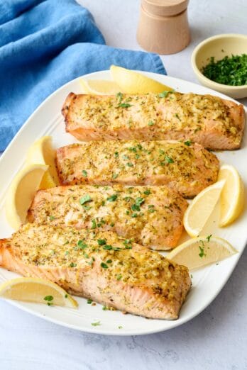 Baked salmon on a platter garnished with chopped parsley and lemon wedges.