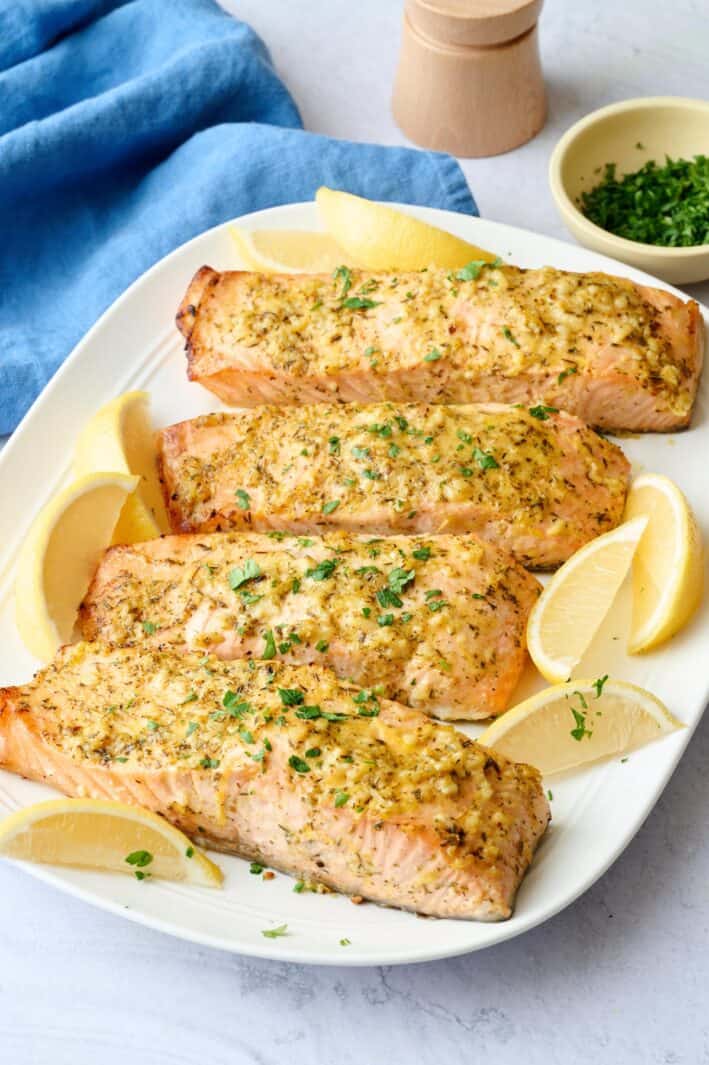 Baked salmon on a platter garnished with chopped parsley and lemon wedges.