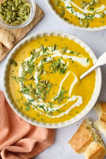 Creamy curried butternut squash soup recipe in a bowl with a swirl of coconut milk and pumpkin seeds on top.