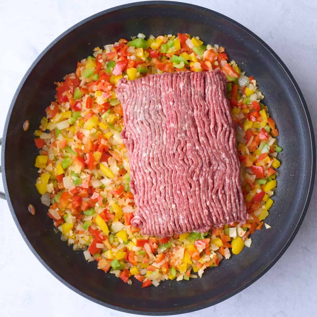 Onions and peppers with garlic in a skillet after cooking with lean ground beef added on top.