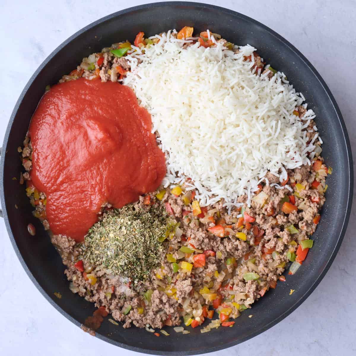 Ground beef and veggies after cooking with tomato sauce, cooked rice and seasonings added on top before combining.