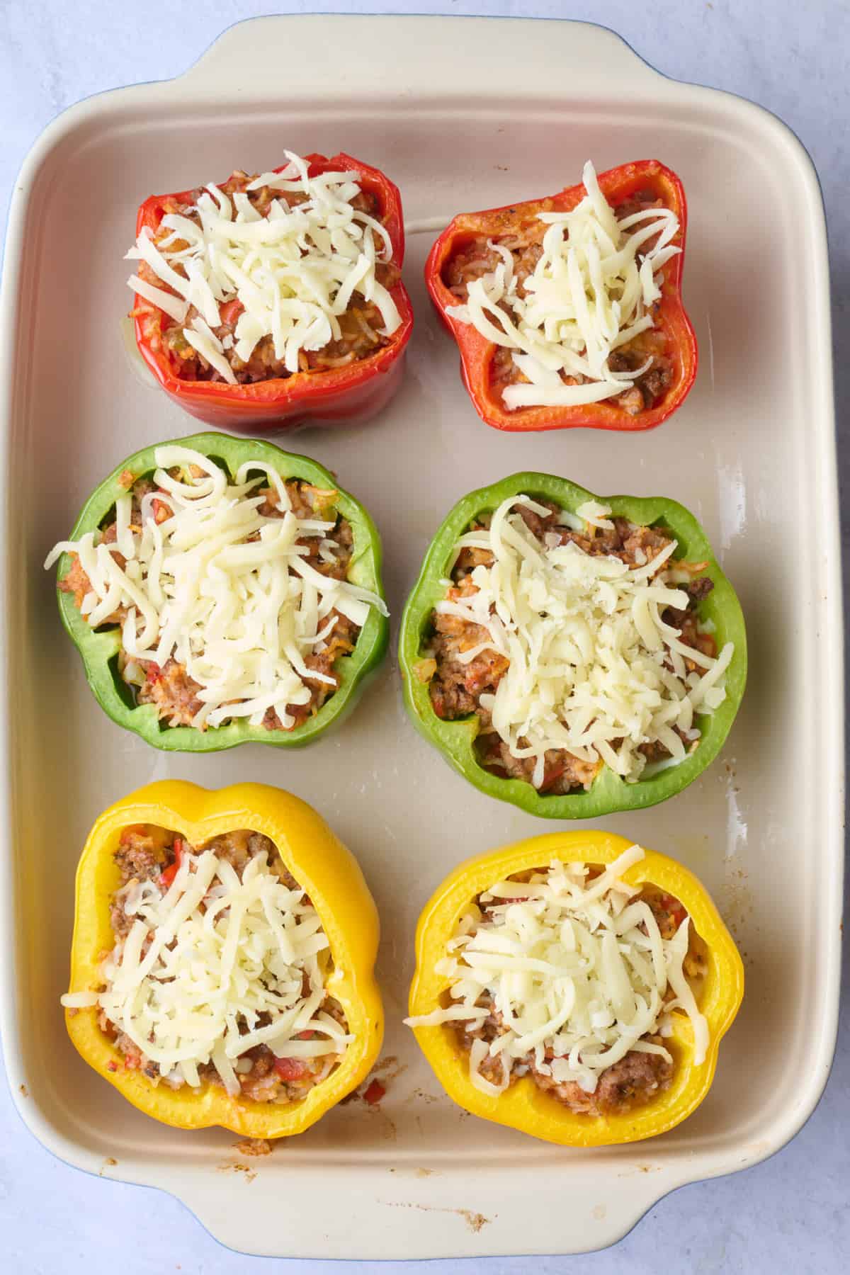 Peppers after stuffing with meat mixture and added to a baking dish with shredded cheese on top before baking.