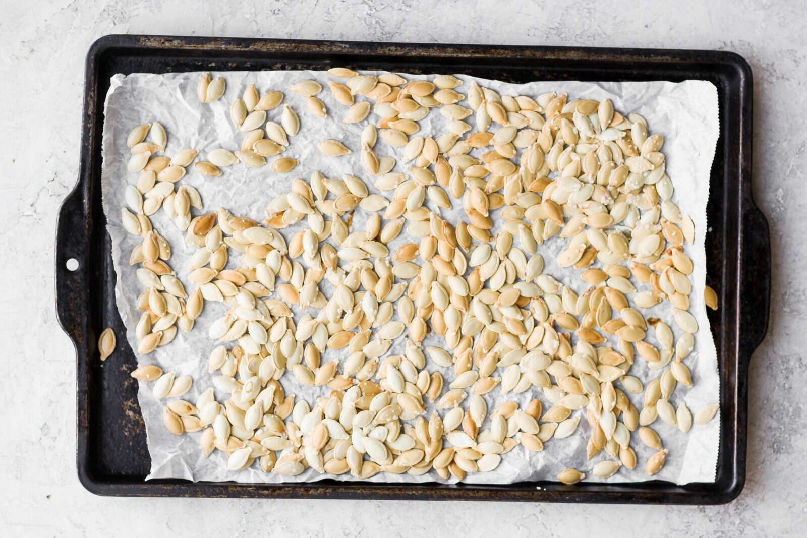 Golden brown roasted pumpkin seeds on a parchment line baking sheet.