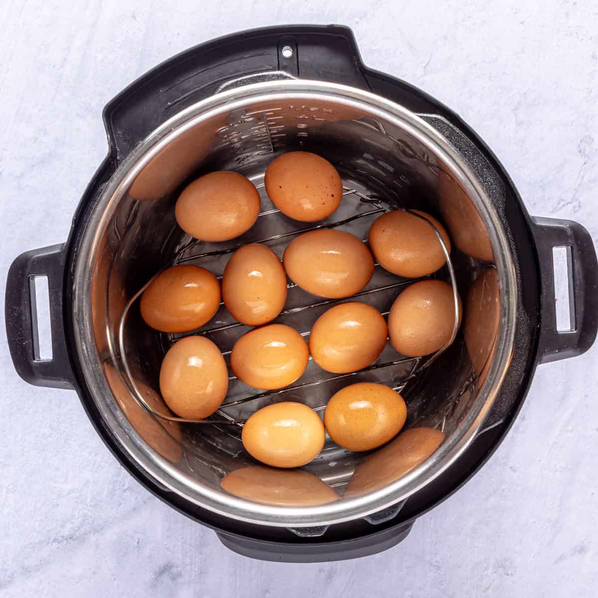 Twelve eggs and a small amount of water in an instant pot on a wire egg rack.