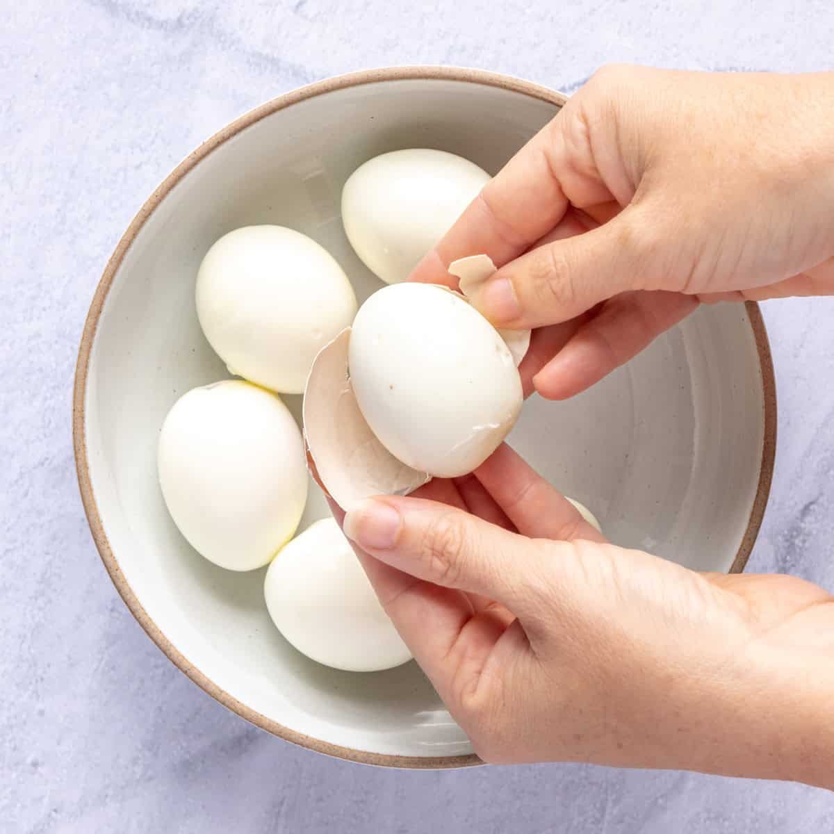 Hands peeling shells from boiled eggs.