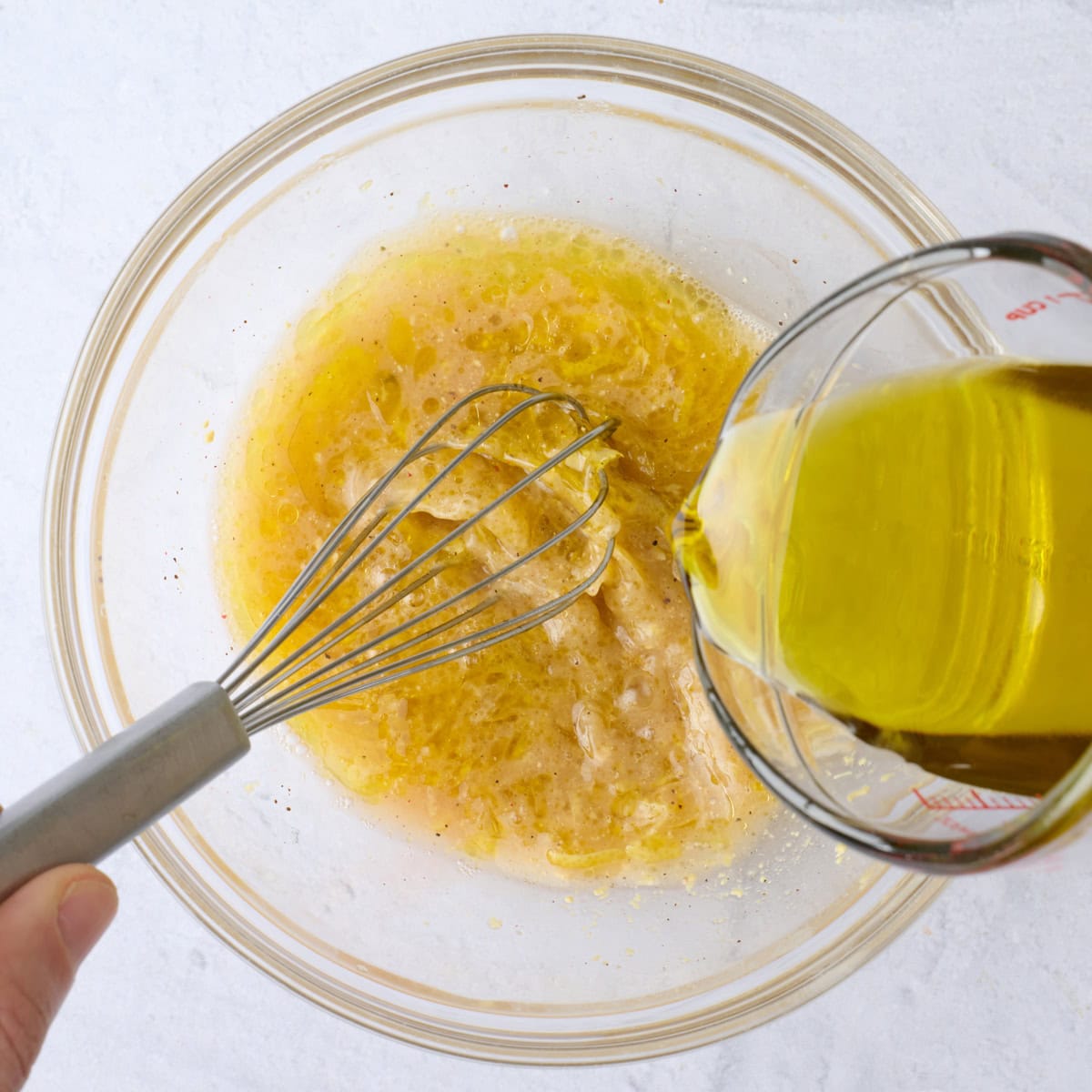 Lemon vinaigrette being whisked with oil being poured in at the same time.