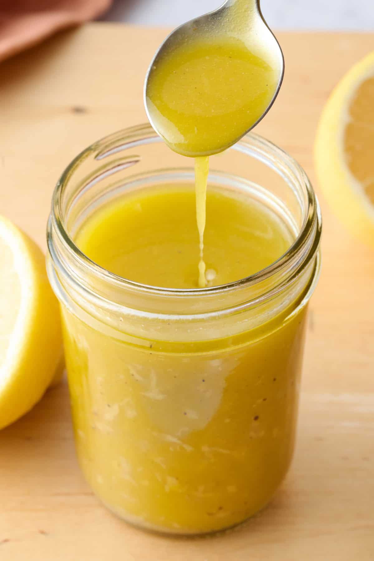 The best lemon vinaigrette recipe being drizzled into a small jar with a spoon.