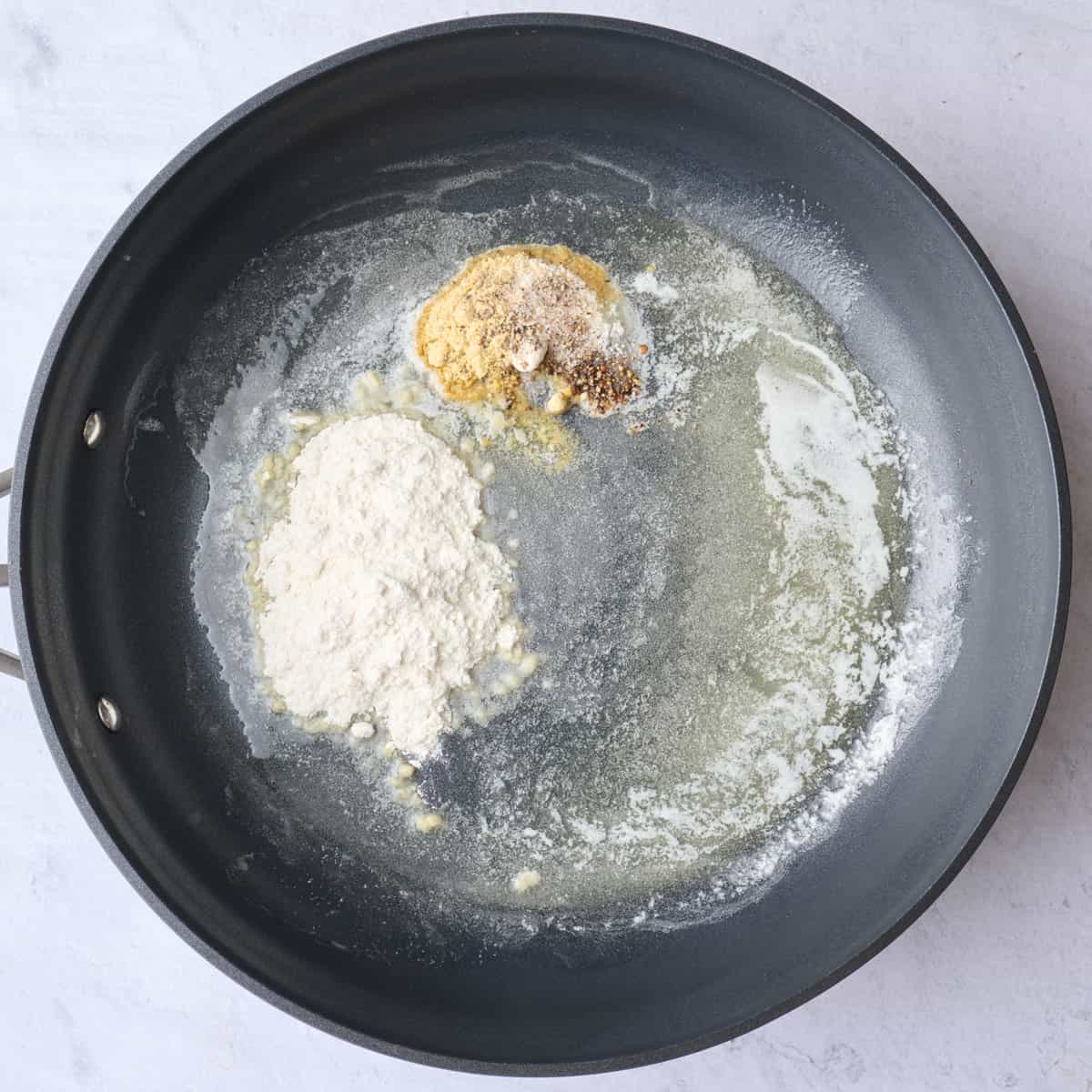 Melted butter in a large saucepan with flour, garlic and mustard powder, salt and pepper added to make roux for cheese sauce.