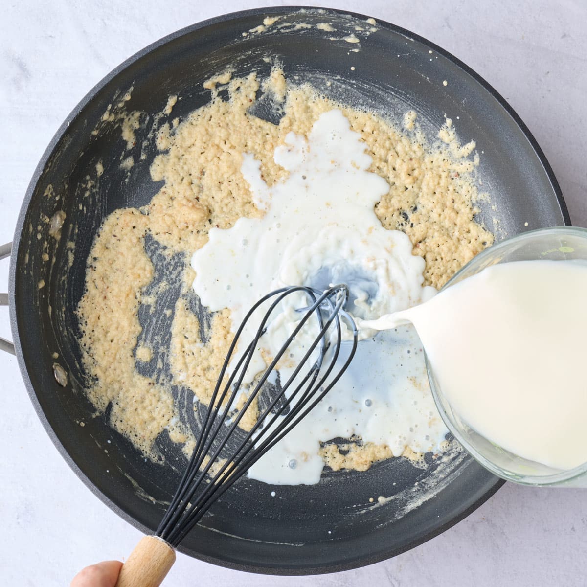 Milk being poured into roux and whisked to create the mac and cheese sauce.