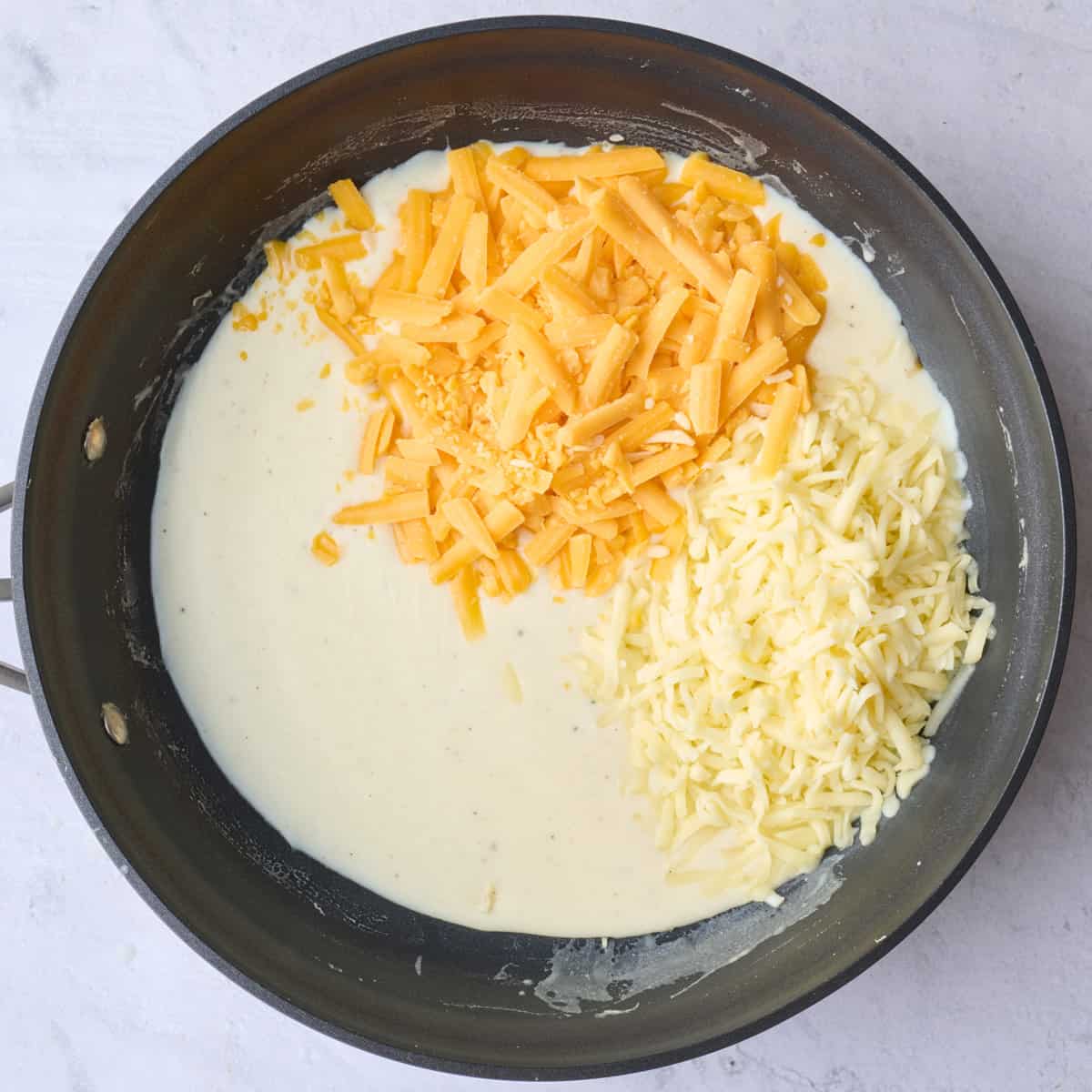 Two types of shredded cheese added into thickened milk sauce before combining.