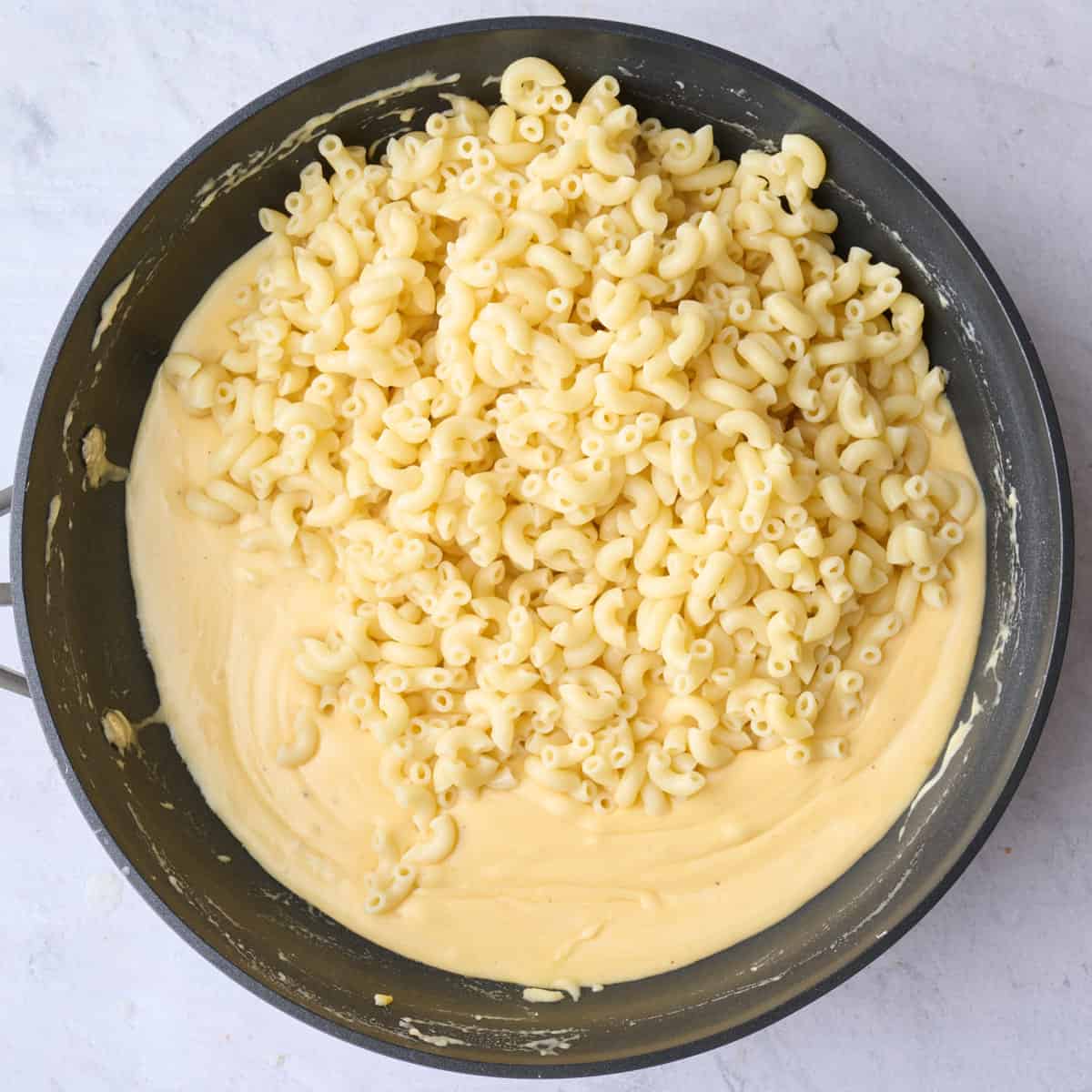 Cheesy sauce in a pot with cooked elbow pasta added before combining to recipe.