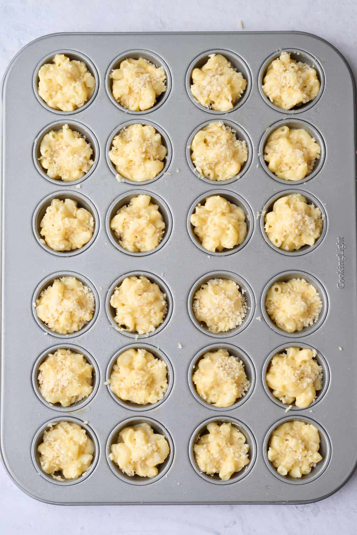 Mac and cheese divided into a mini muffin pan and topped with breadcrumbs before baking.