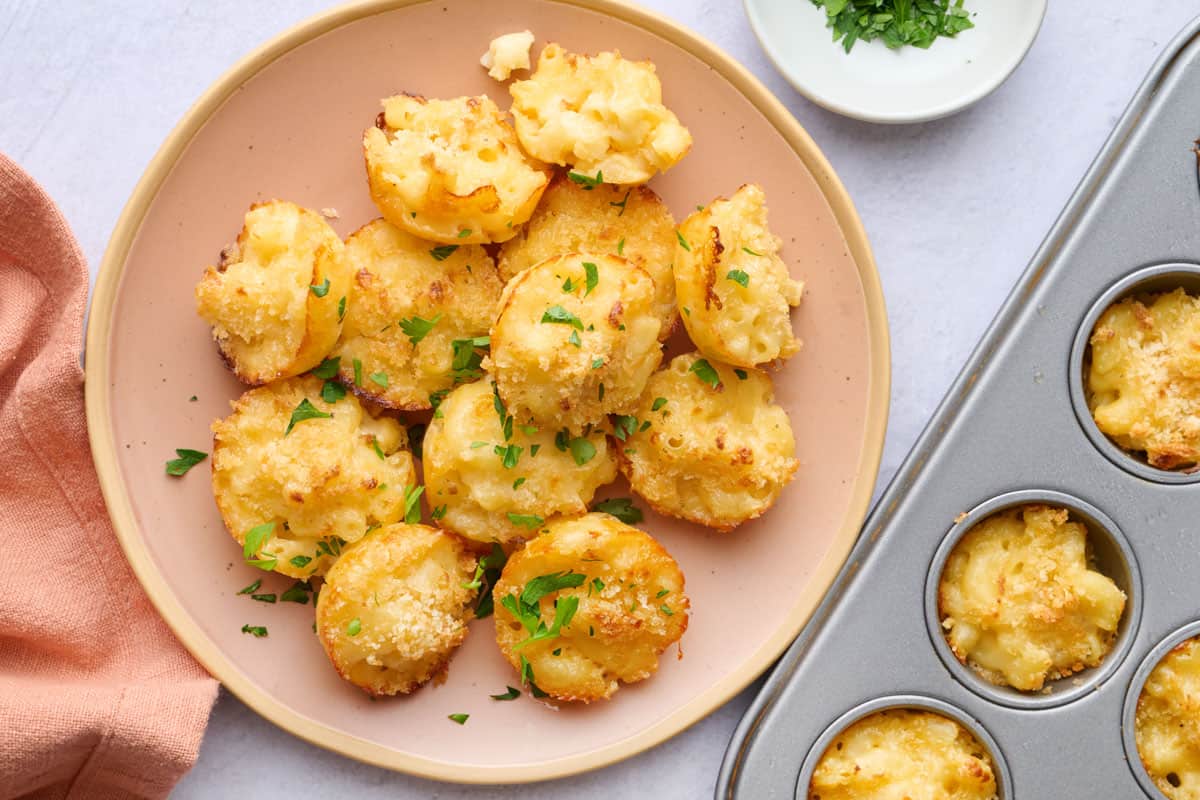 Homemade mac and cheese bites on a plate with a mini muffin pan nearby.