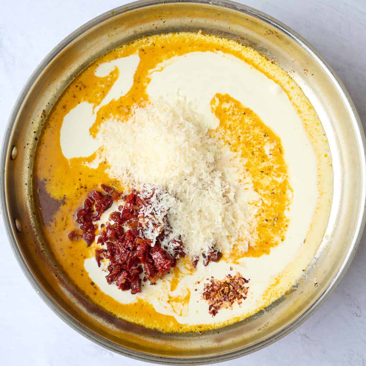 Heavy cream, tomatoes, parmesan, and red pepper flakes added to other sauce ingredients before combining.