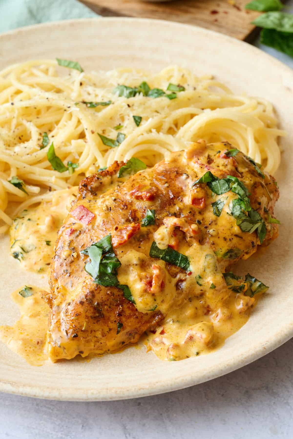 Marry me chicken breast on a plate with extra sun dried tomato sauce spooned on top served with pasta.