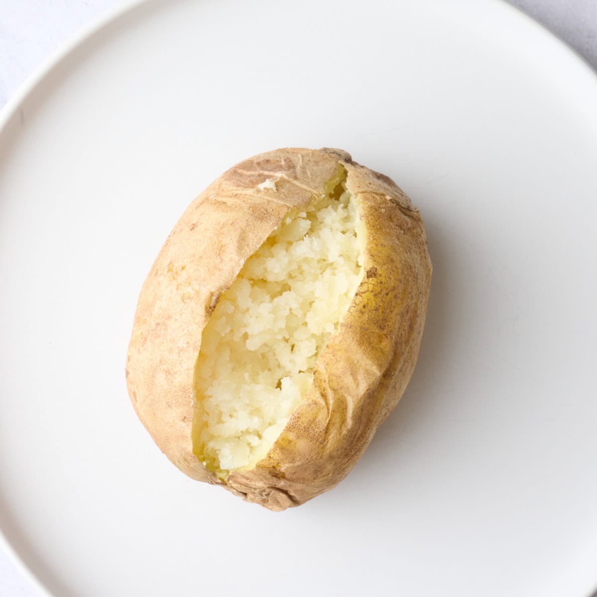 Microwaved baked potato on a plate after slicing open and fluffy insides.
