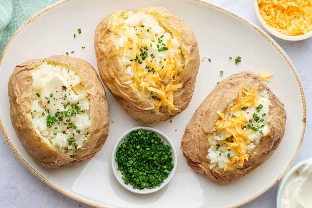 Microwaved baked potato recipe on a platter, open and fluffed with butter and shredded cheese on top.