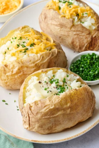 Microwave baked potatoes on a platter after fluffy and garnished with a mix of butter, chives, shredded cheese and sour cream.