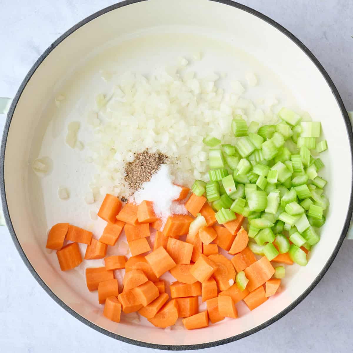 Chopped carrots, onions, and celery in a pot with salt and pepper before cooking.
