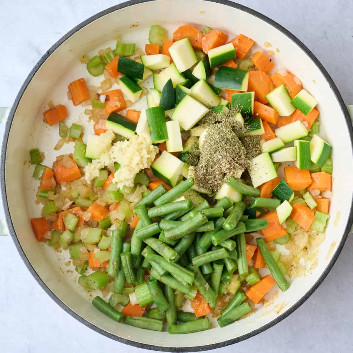 A pot of vegetables in a pot with spices and minced garlic for soup recipe.