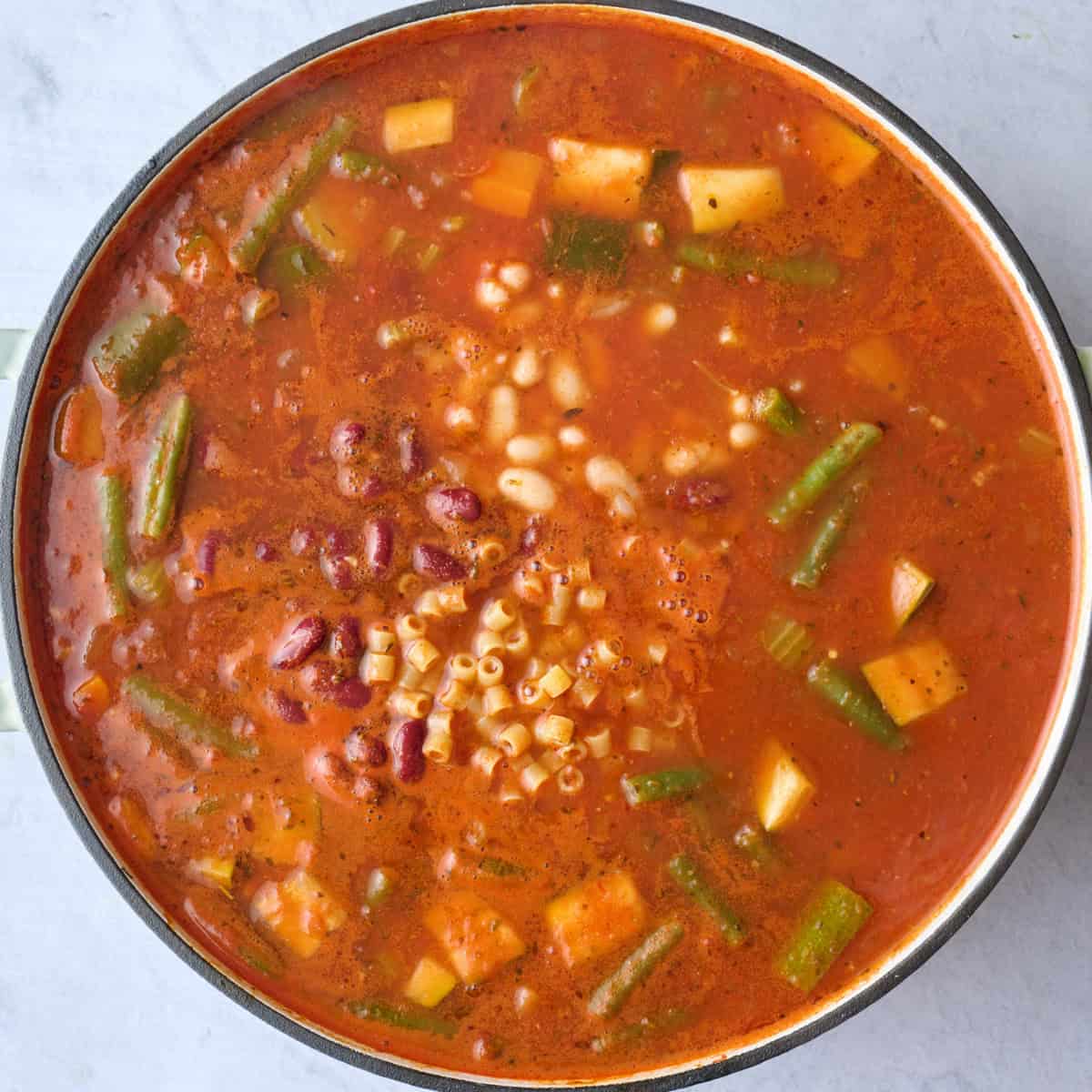 Minestrone soup base in a pot after simmering with beans and dry pasta added.