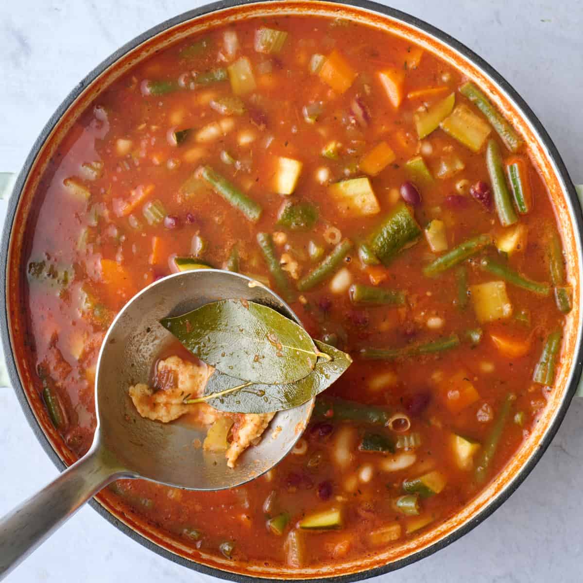 A ladle lifting up bay leaves from soup to discard after cooking.