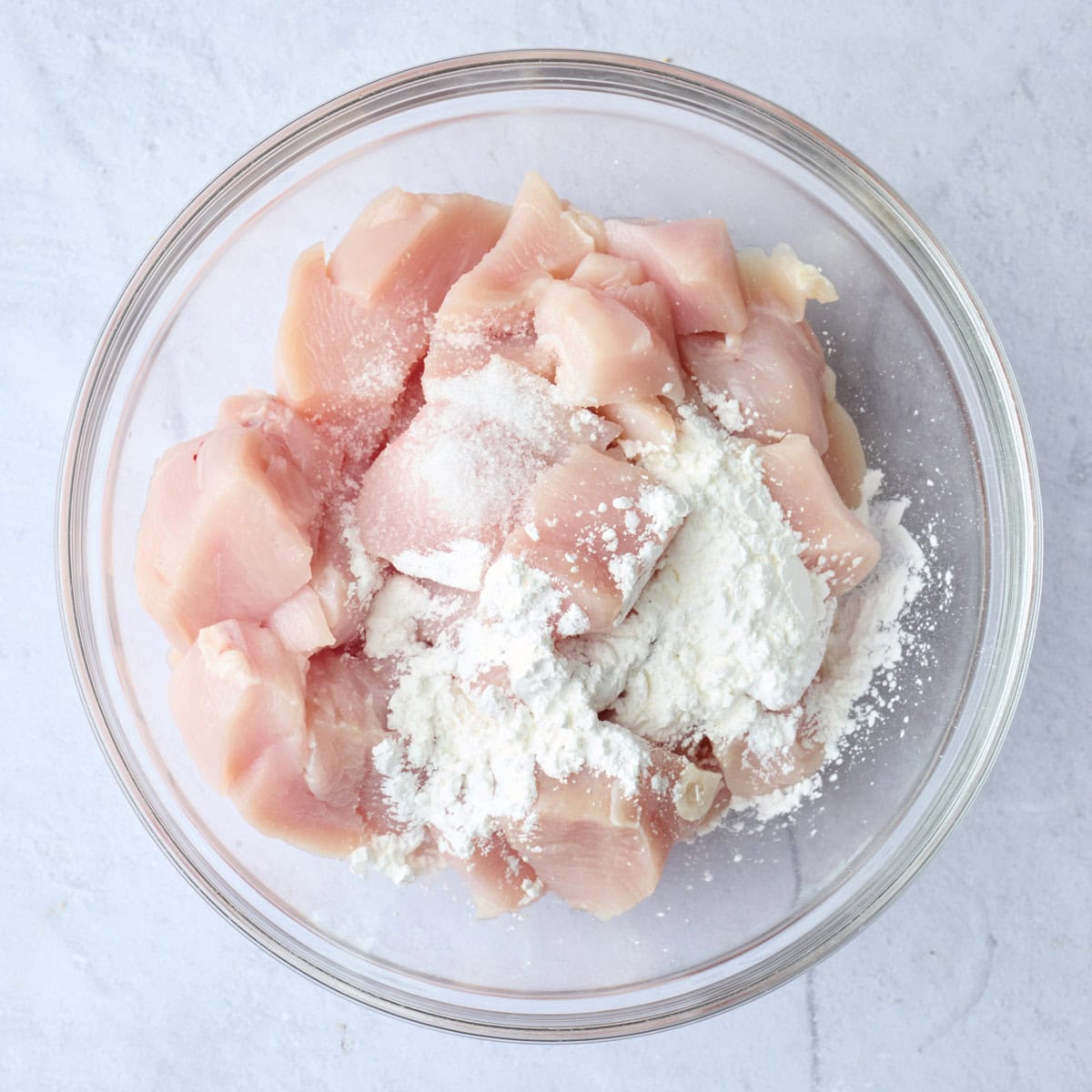 Chicken pieces in a bowl with cornstarch and salt added before tossing.