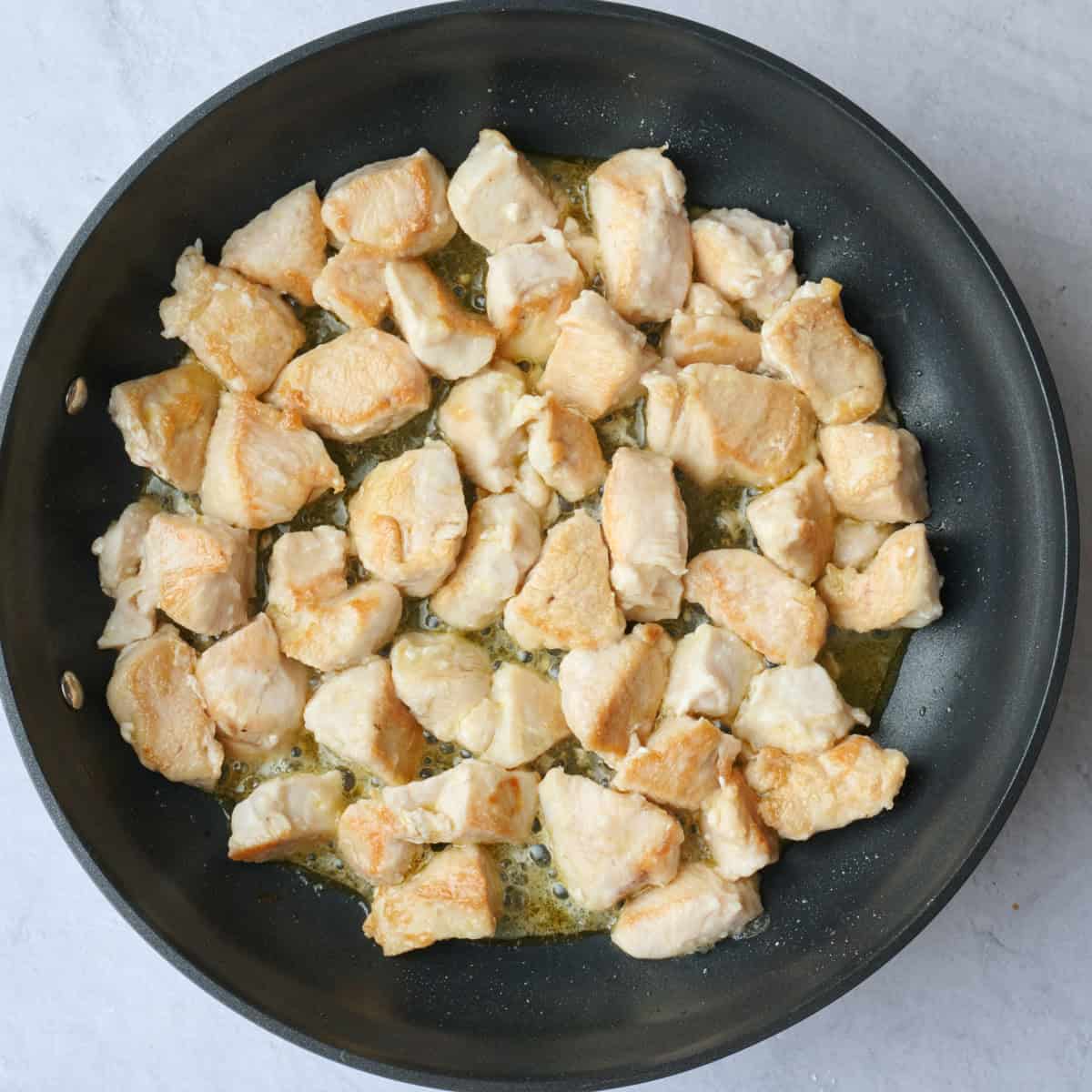 Chicken bites in a skillet after flipping.