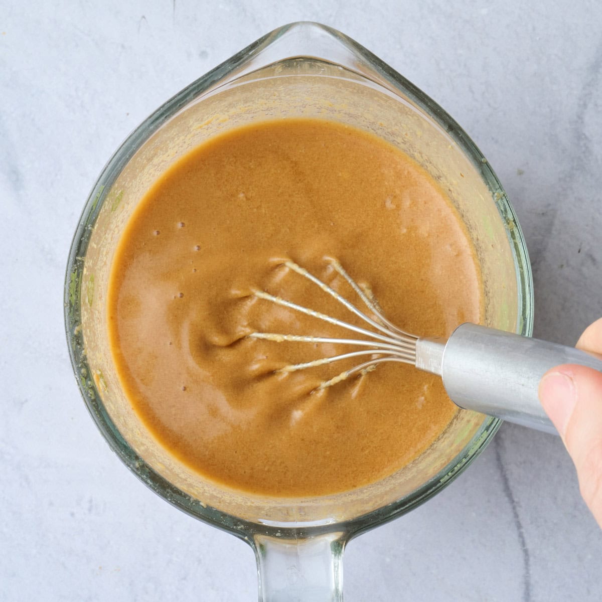 Peanut butter sauce being whisked in a measuring cup.