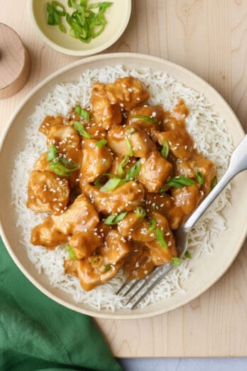 Peanut butter chicken served over white rice and garnished with sliced green onions and sesame seeds.