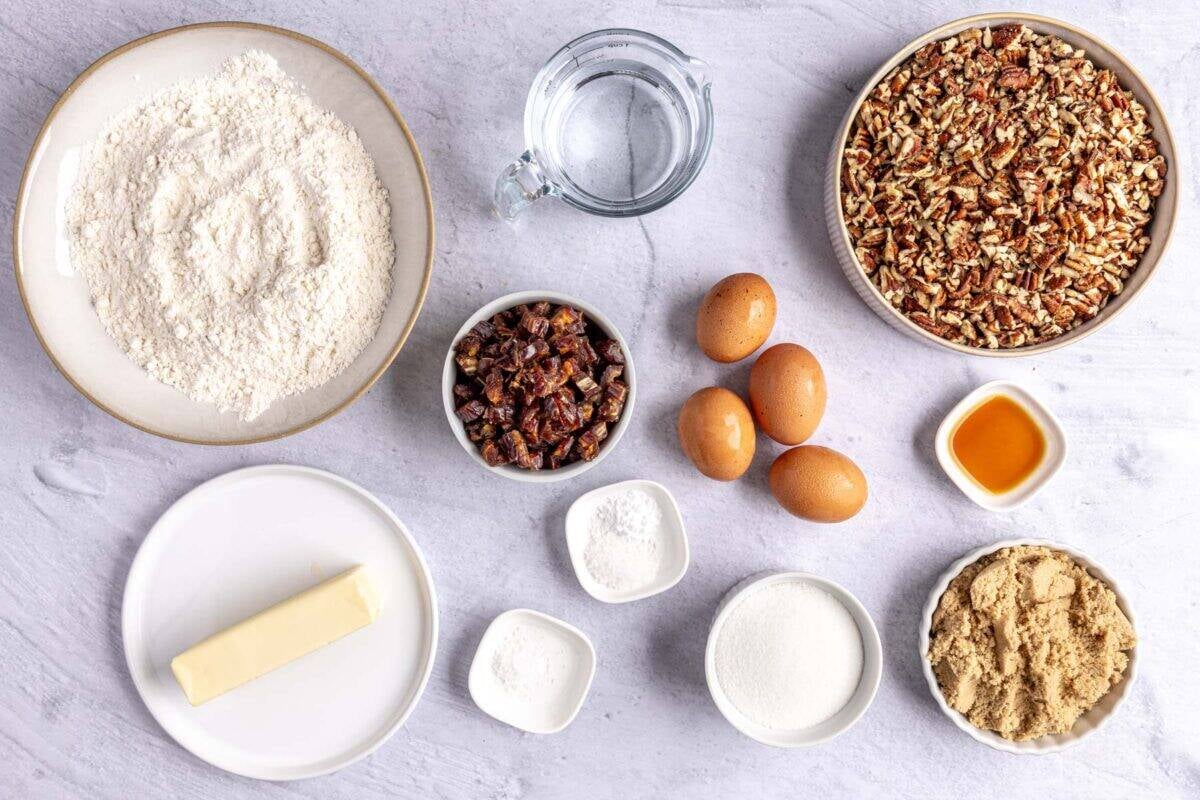 Ingredients for dessert recipe: flour, pecans, water, dates, butter, baking soda, salt, eggs, sugar, brown sugar, and vanilla extract.