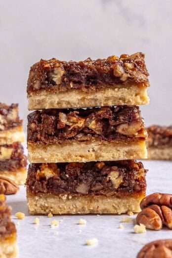 Homemade pecan pie bars made with dates stacked up to show gooey pecan filling and thick crust.