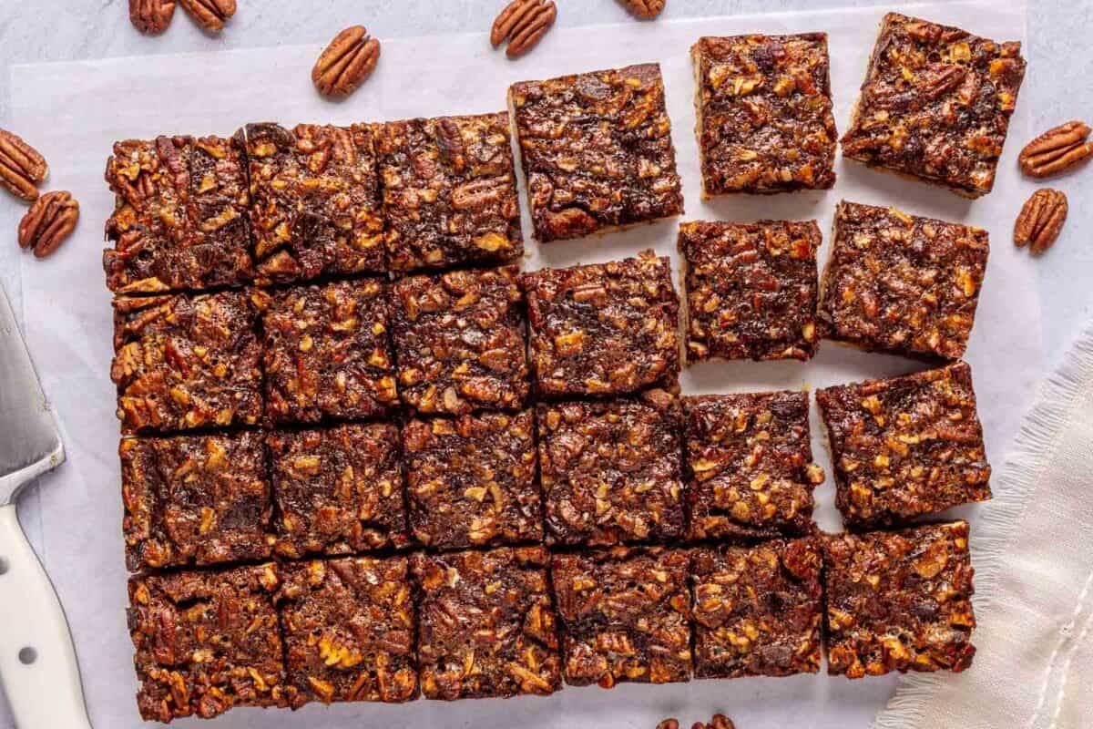 Homemade pecan pie bars made with dates on parchment paper after cutting with extra pecan halves around.