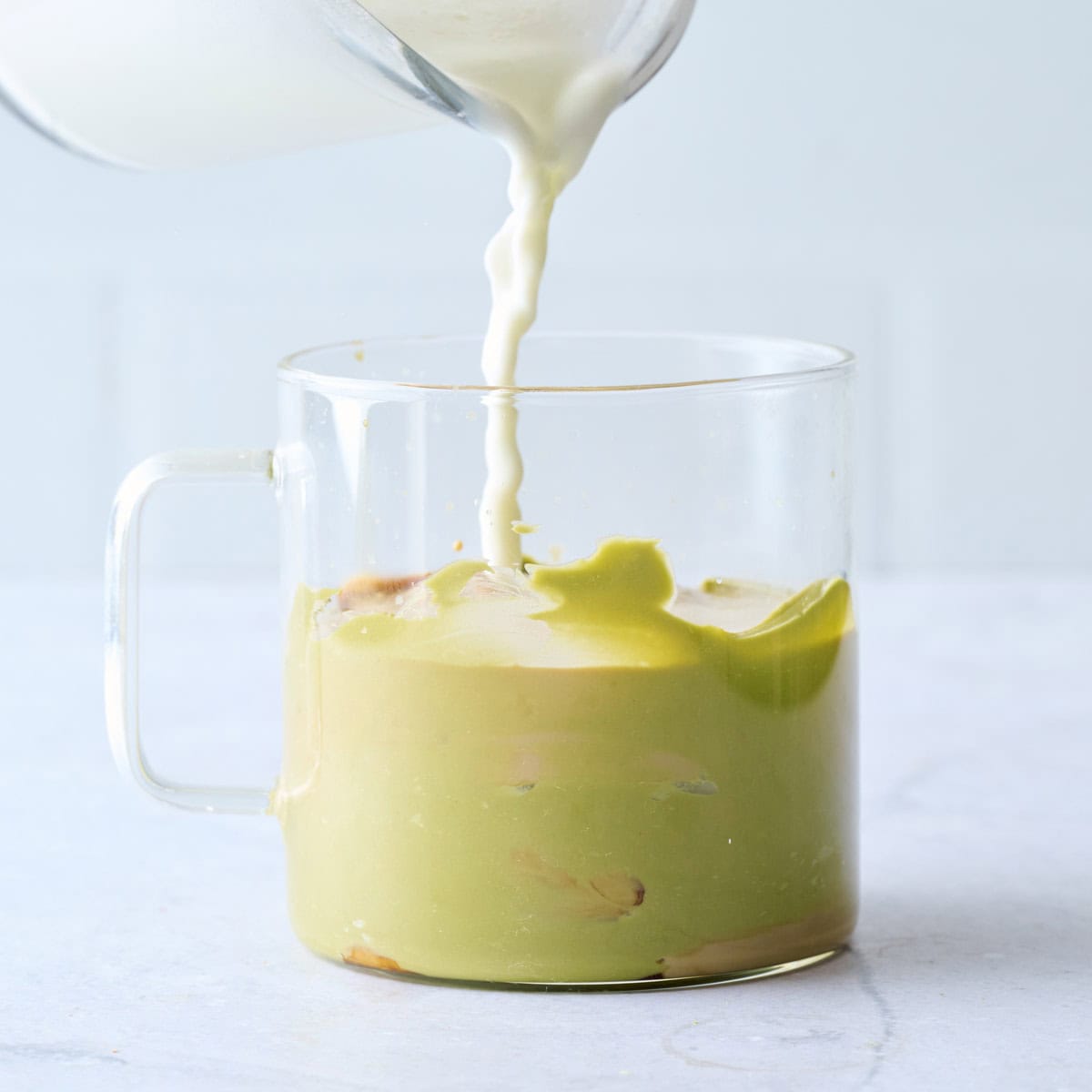 Milk being poured into a glass mug with espresso and pistachio cream.