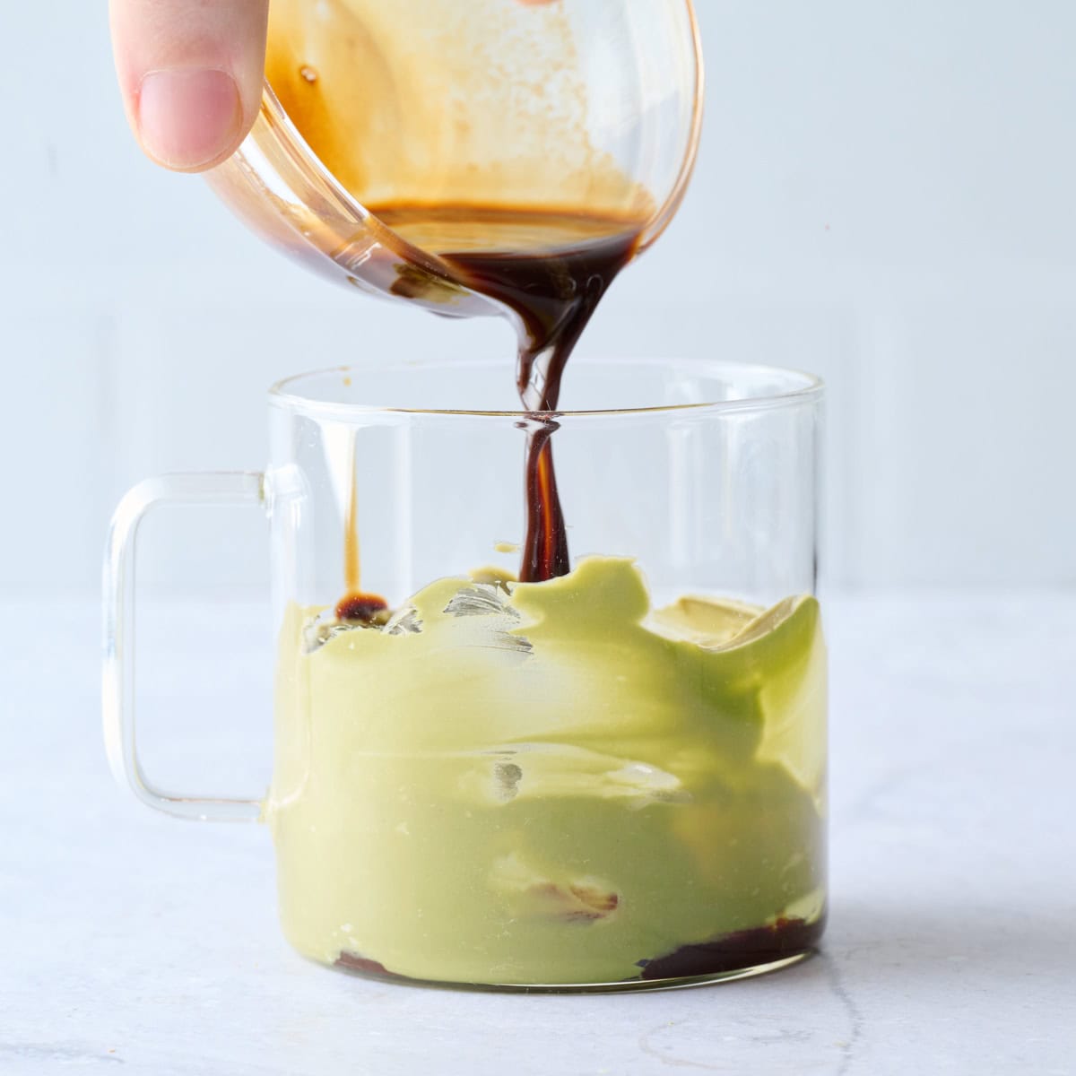 Espresso being poured into a glass mug with pistachio butter smeared on the sides for latte recipe.