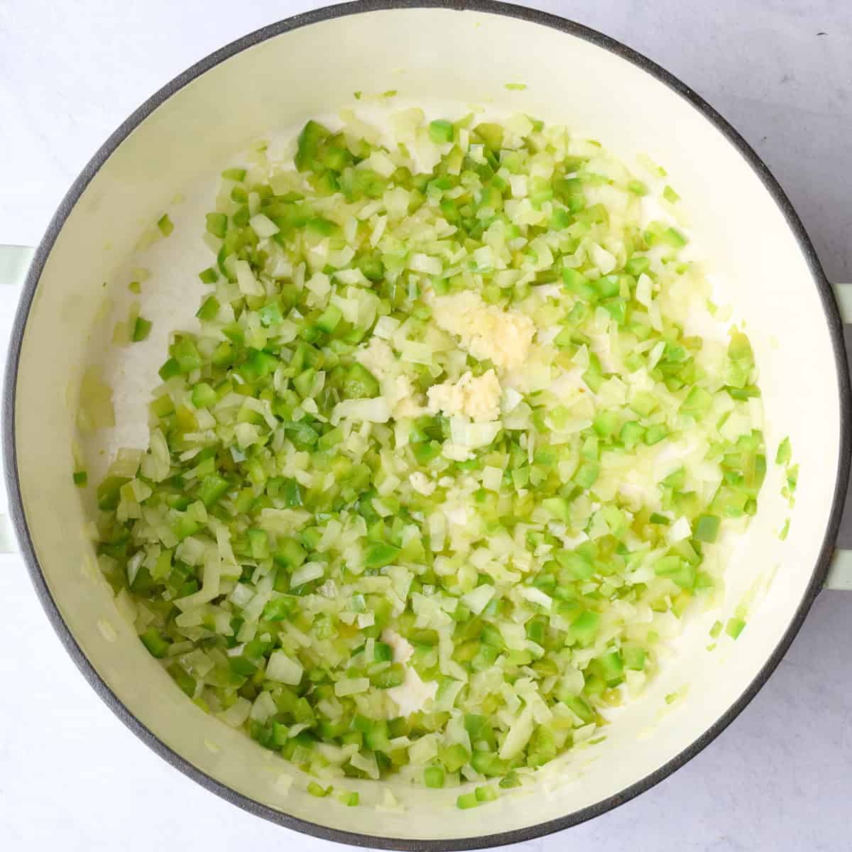 Cooked onion and green pepper in pot with garlic added on top for chili recipe.