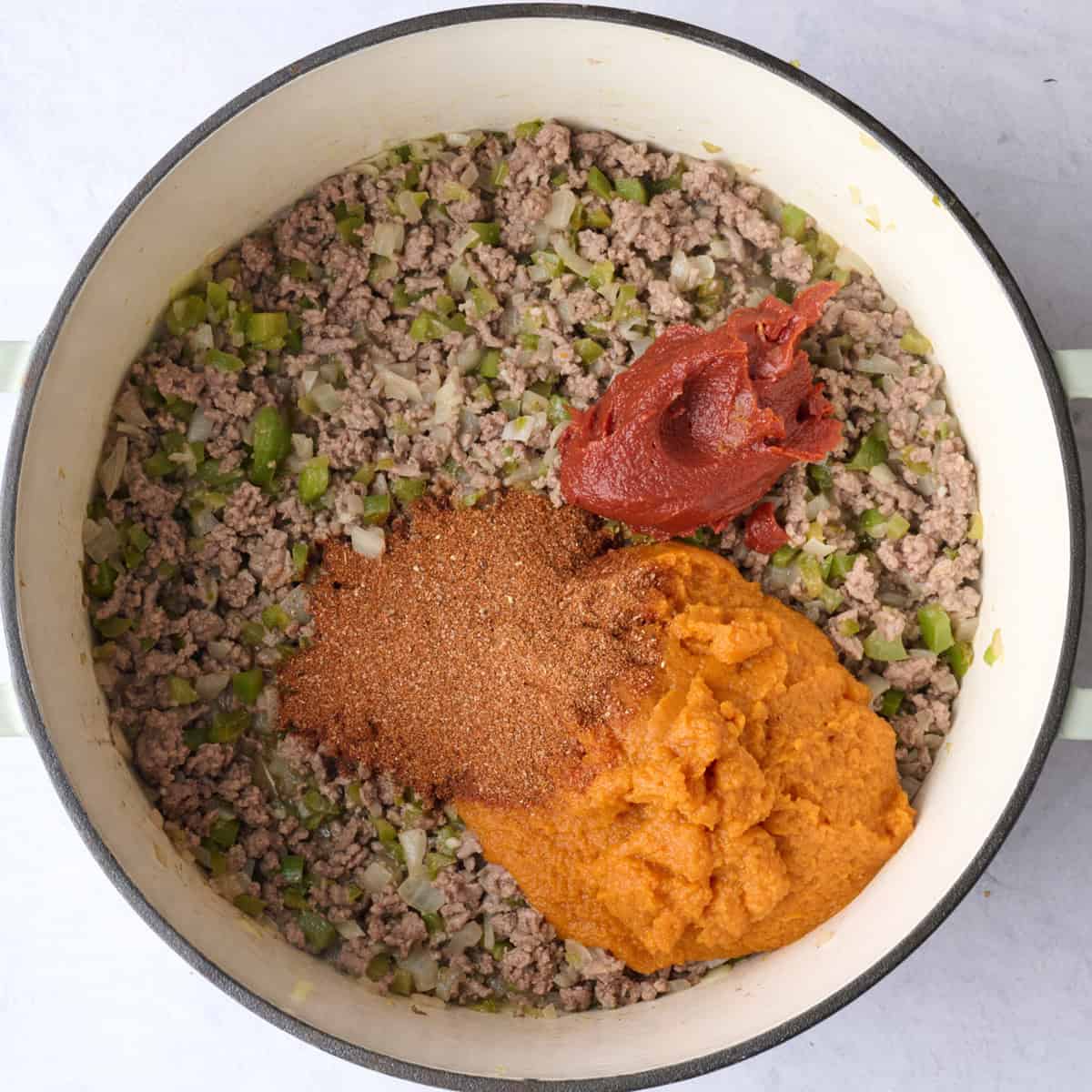 Pumpkin puree, tomato paste and chili seasonings added to pot with cooked ground beef, peppers and onions.
