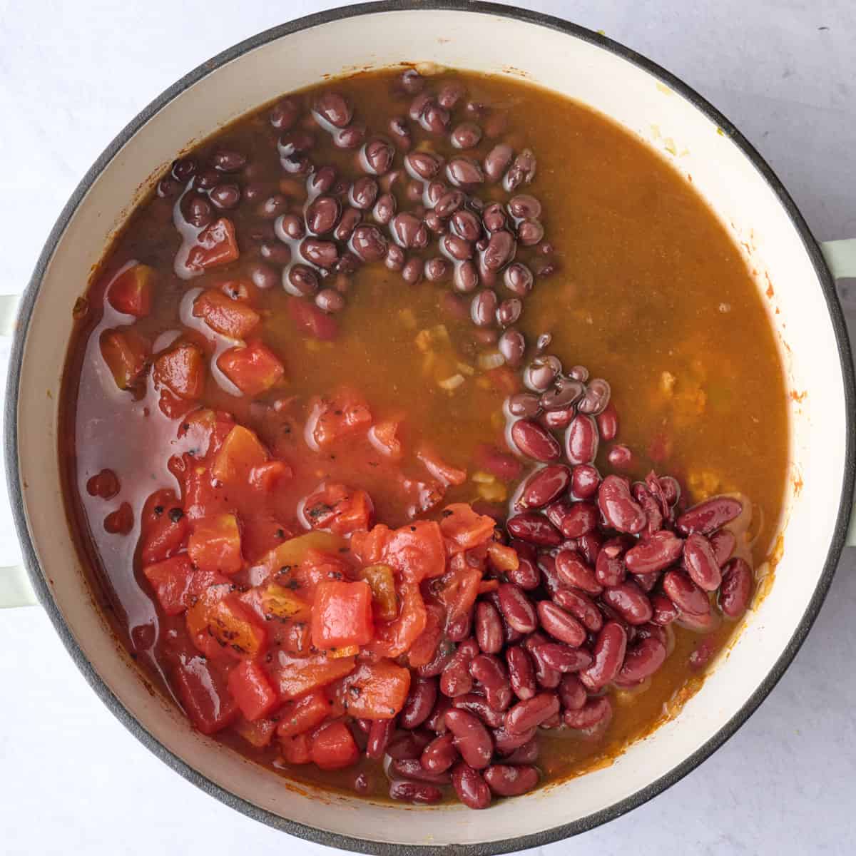 Fire roasted tomatoes, black beans, kidney beans, and broth added to pumpkin chili base in a pot before combining.