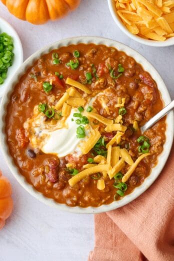 Pumpkin puree chili recipe served in a bowl and topped with sour cream, shredded cheddar cheese and green onions.