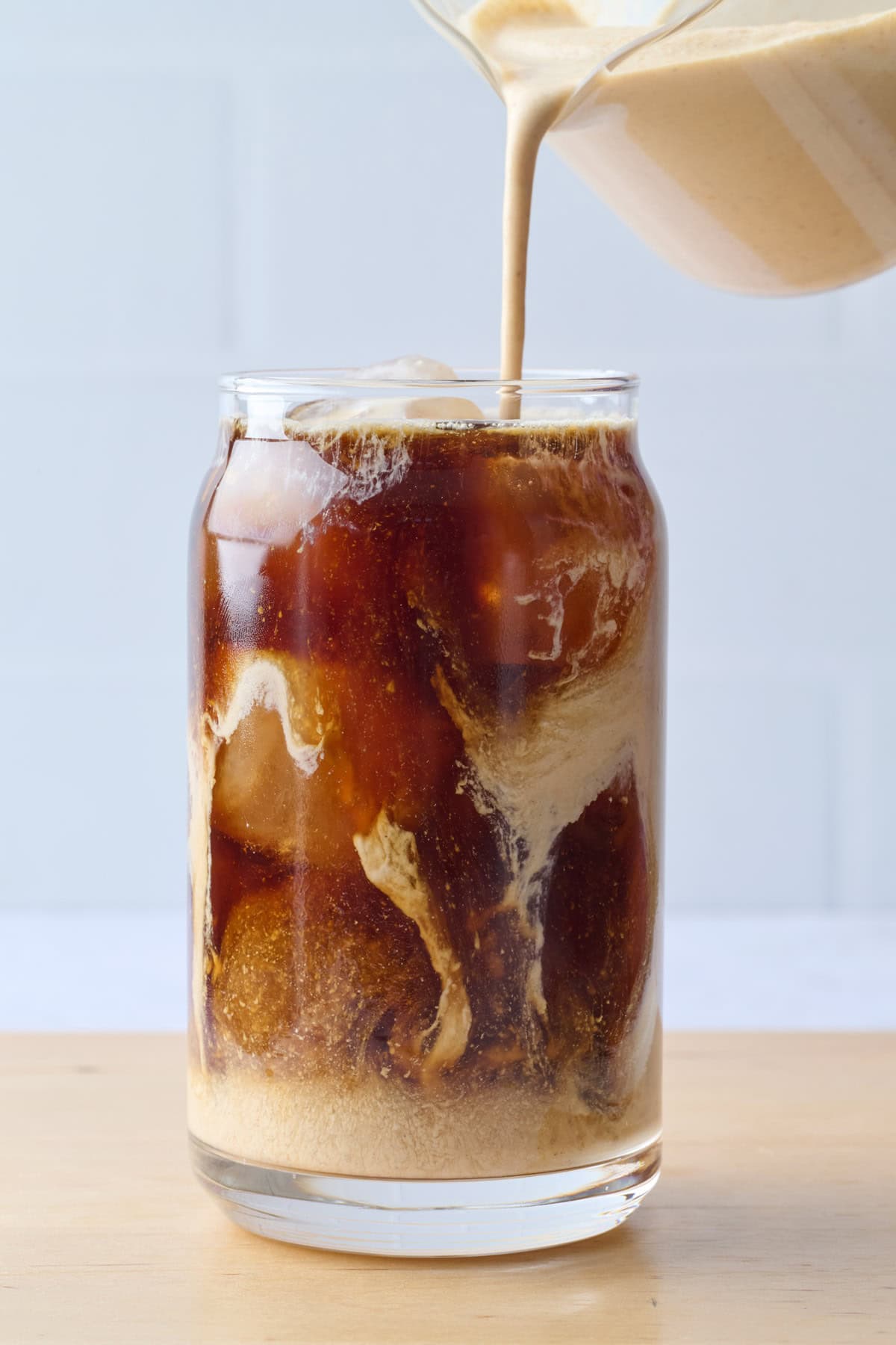 Homemade pumpkin cream being poured into a glass with ice and cold brewed coffee.