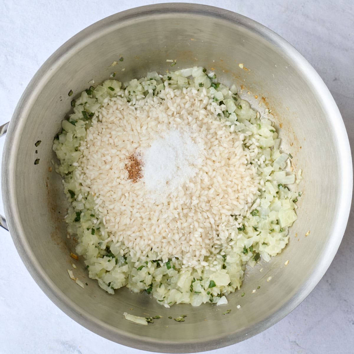 Arborio rice, salt and nutmeg added on top of onion mixture for risotto recipe.