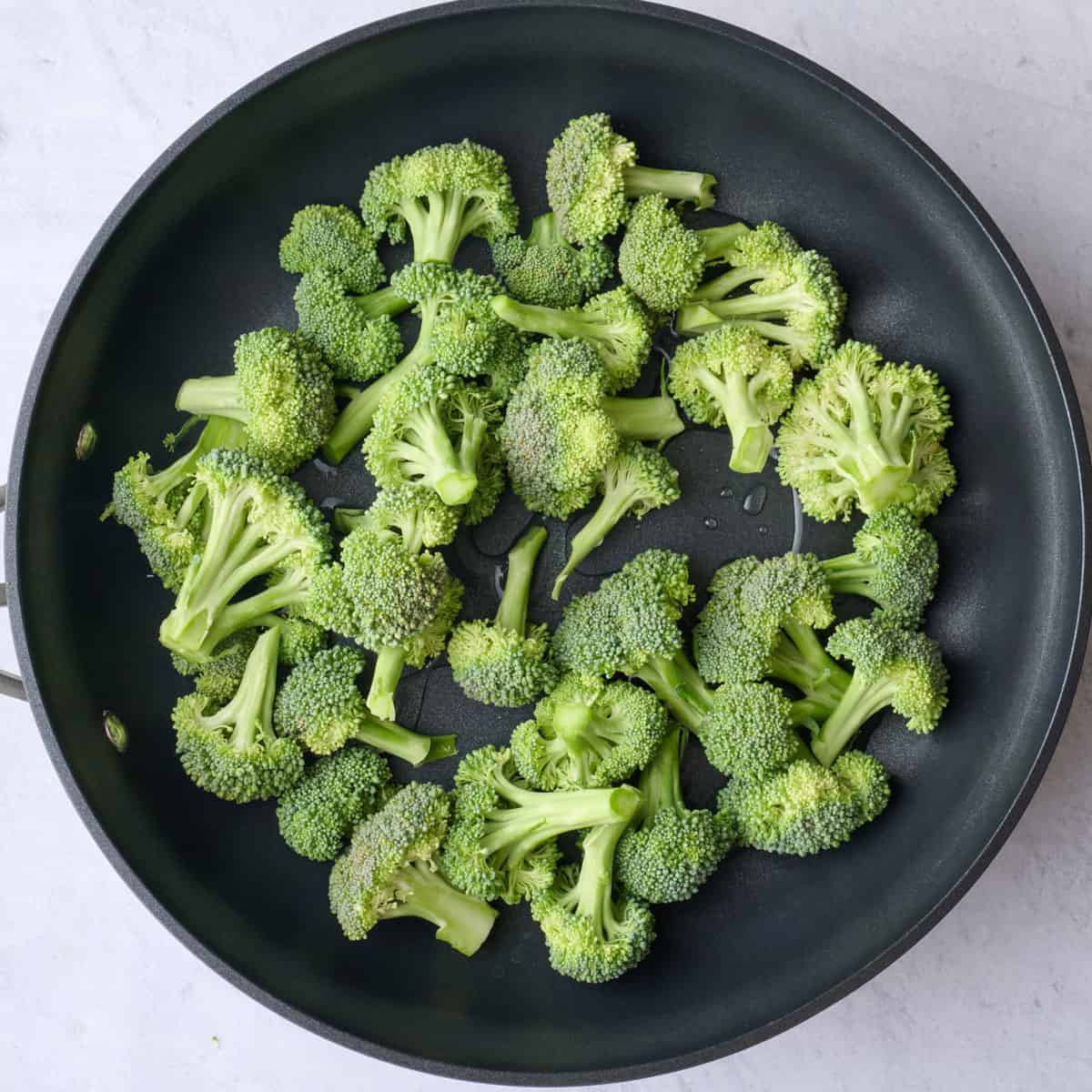 Broccoli florets and water in a skillet before cooking.