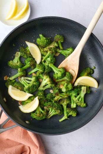 Best sauteed broccoli with garlic in a plan with lemon wedges.