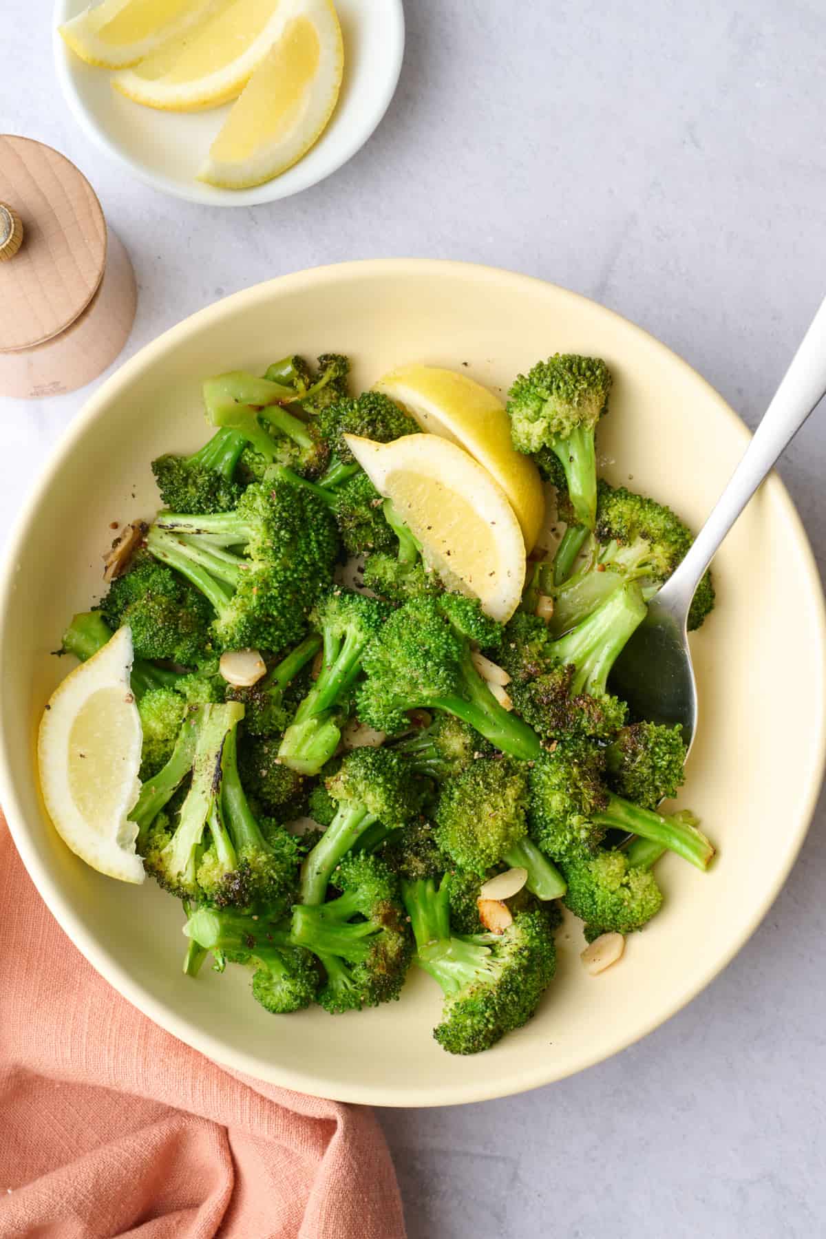 Easy sauteed broccoli recipe in a serving bowl with lemon wedges.