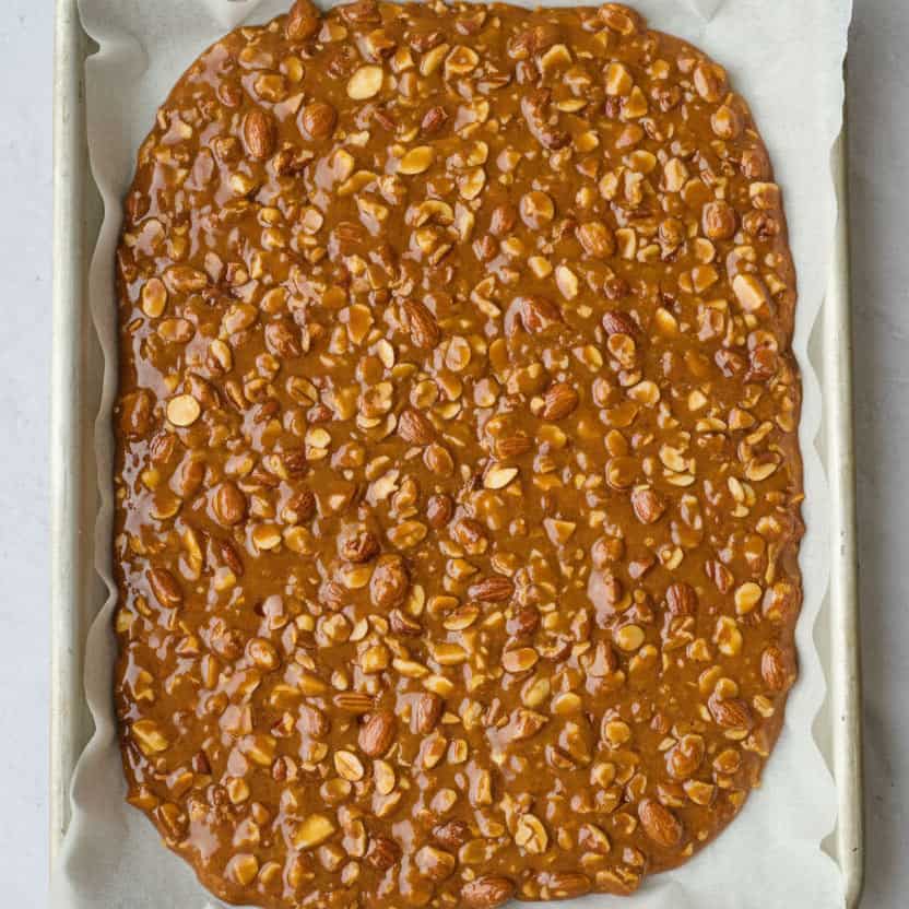 Hot almond brittle mixture spread into an even layer before hardening.