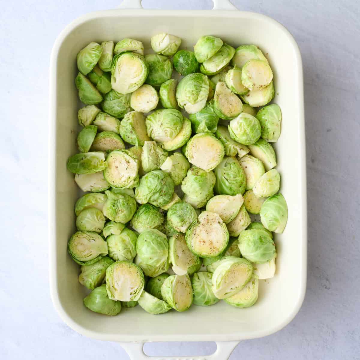 Halved brussel sprouts in a casserole dish after tossing with oil and seasonings before baking.
