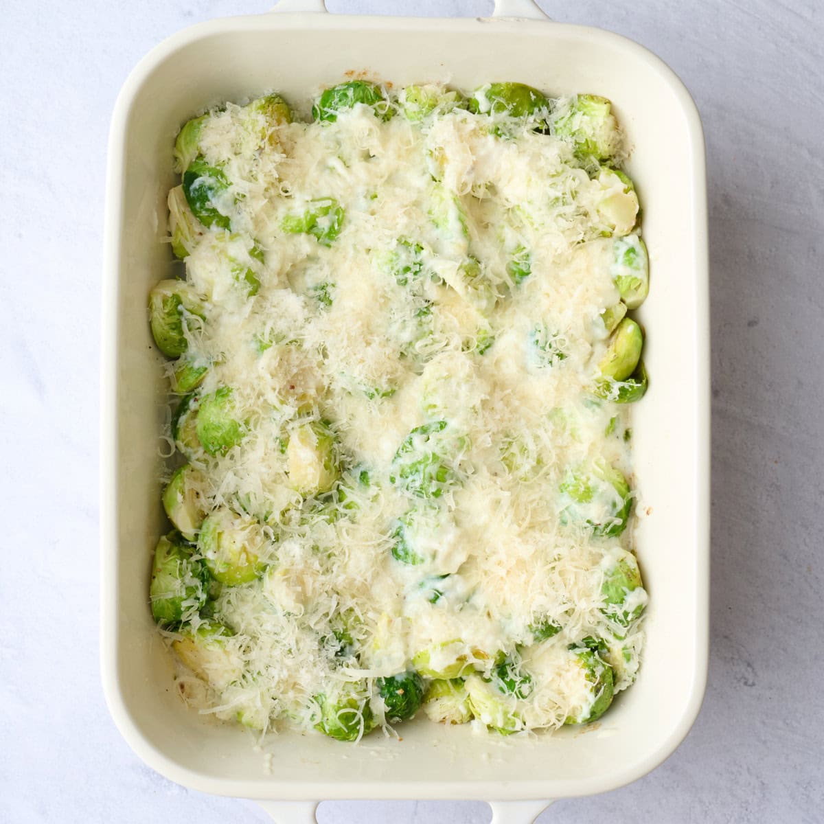 Mornay sauce poured over roasted brussel sprouts in a casserole dish with extra parmesan on top.